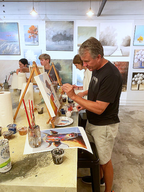 A guest at a Thomas Andrew Art private paint party finishing her canvas